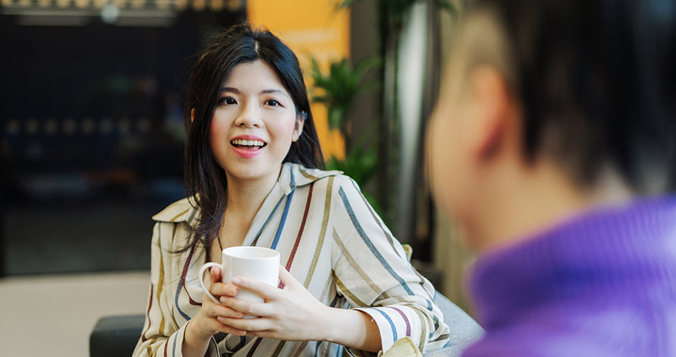 A woman holding a mug talks to a man