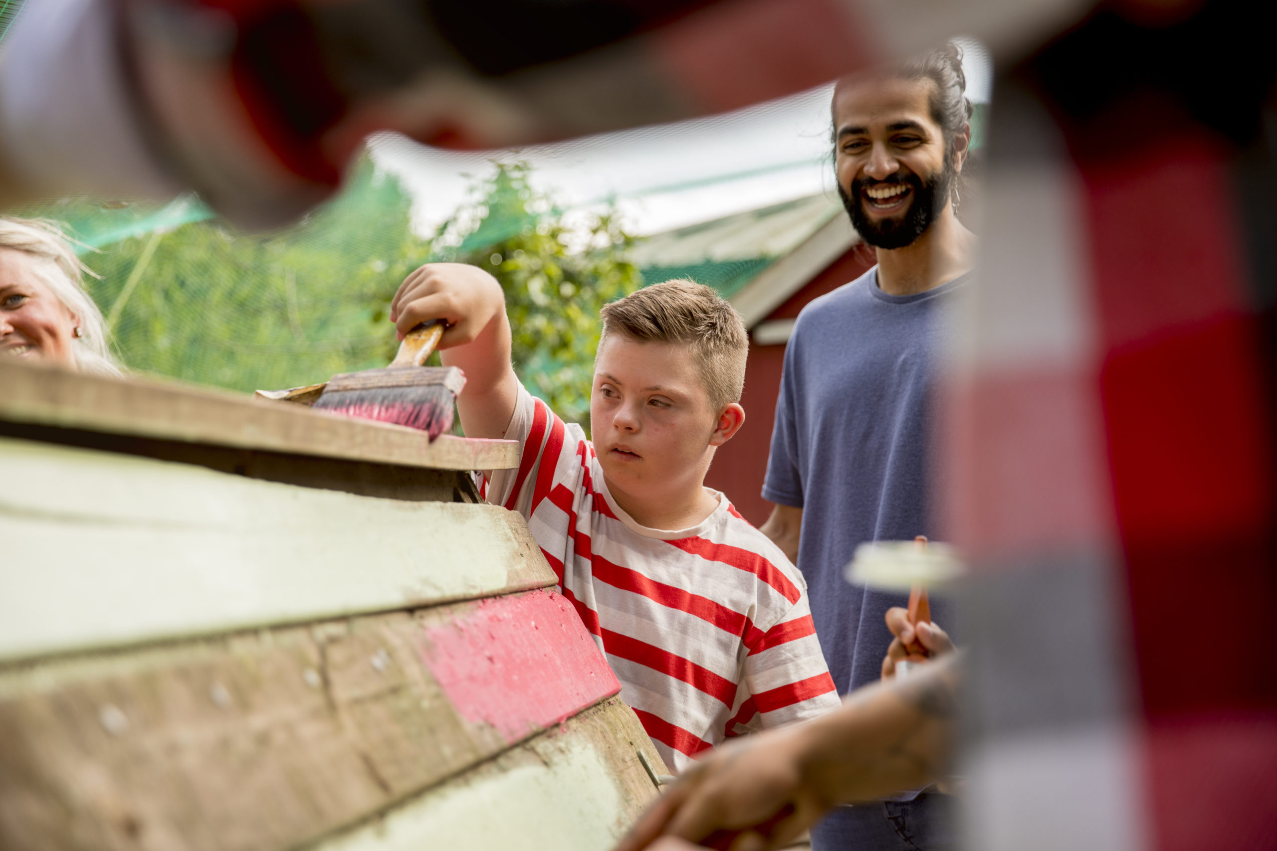 A boy with Down's Syndrome paints a shed whilst a smiling man watches