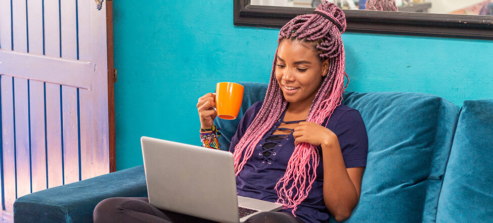 Woman sitting on sofa with laptop holding a cup of tea