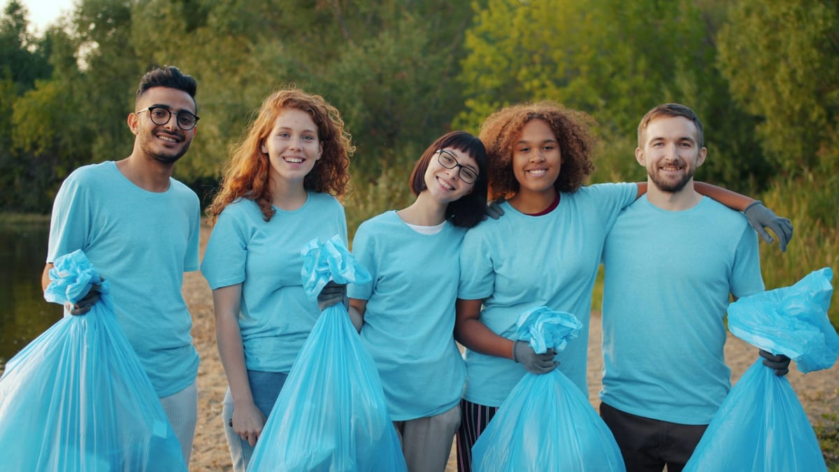 Five young volunteers who have been collecting rubbish with their arms around each other. They're all wearing blue t-shirts and have blue refuse sacks.