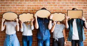 Five people stand against a wall with blank speech bubbles covering their faces