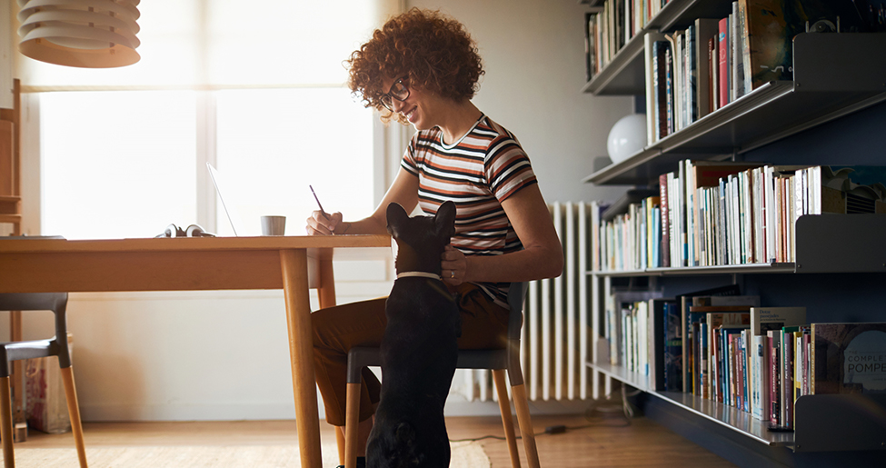 Women sitting at table working flexibly from home with black cat next to her