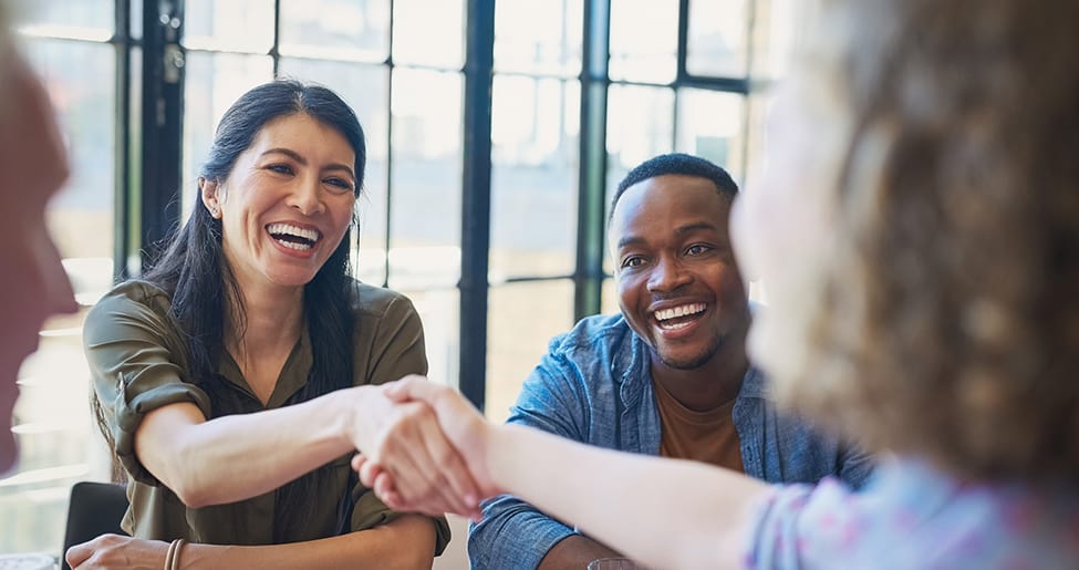 Two people shaking hands while a third looks on