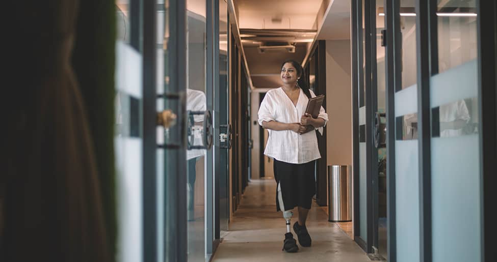 encourage disabled workers to apply: woman with prosthetic leg smiles outside a meeting room, holding a folder.