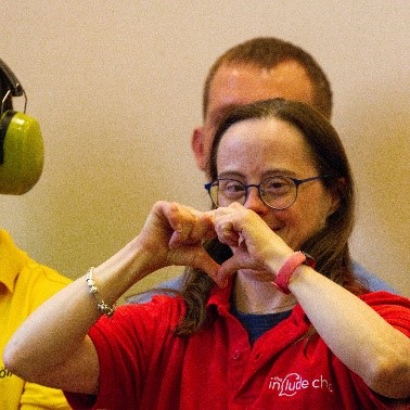 Hannah, Champion at Include.org make a heart shape with her hands.