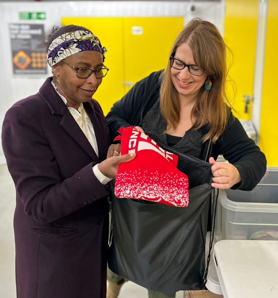 Two ladies from The Separated Child Foundation, holding a black bag and red scarf, inspecting donations from CharityJob.com