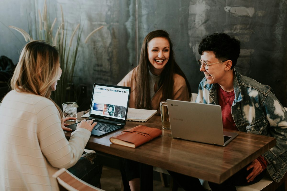 Three colleagues working together at a table with laptops. There is a brown leather journal on the table. Article from CharityJob on inclusive employment.