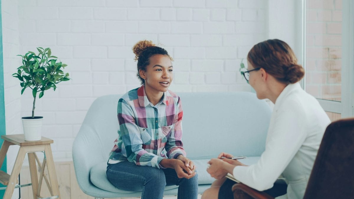 A young woman in a checked shirt is talking a woman who has her back to the camera. Mental health barriers to employment article for CharityJob