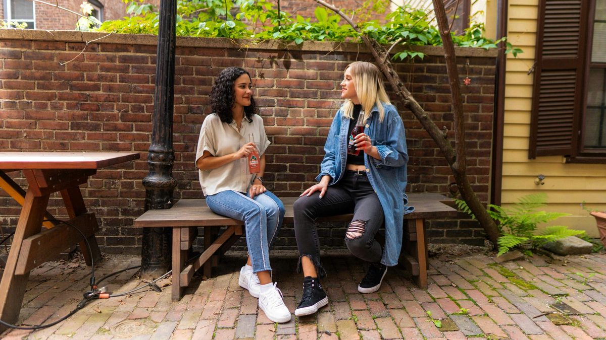 Two women sitting on an outdoor bench and talking. CharityJob article on mental health first aid in the workplace. 
