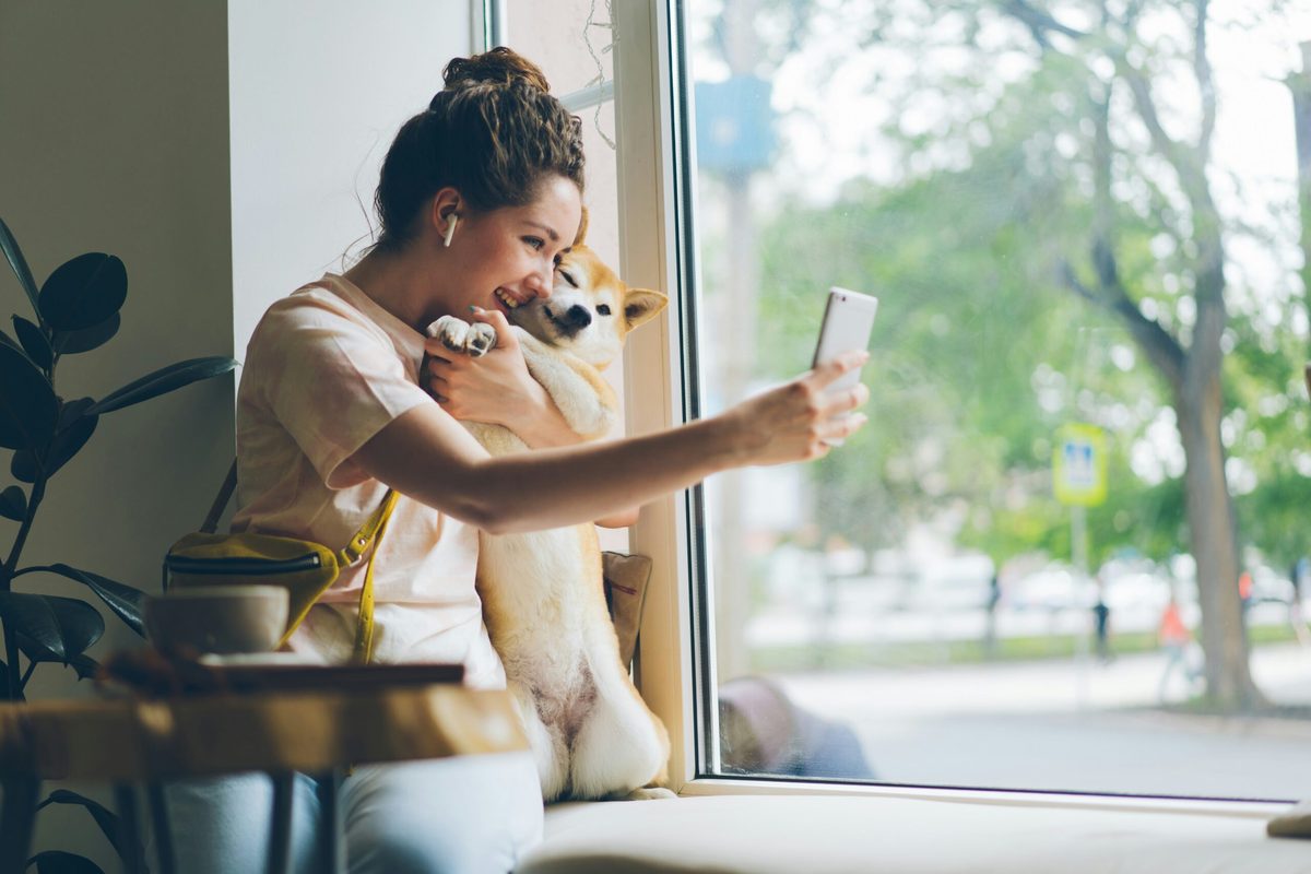 Woman cuddling dog as she films herself on a mobile phone.